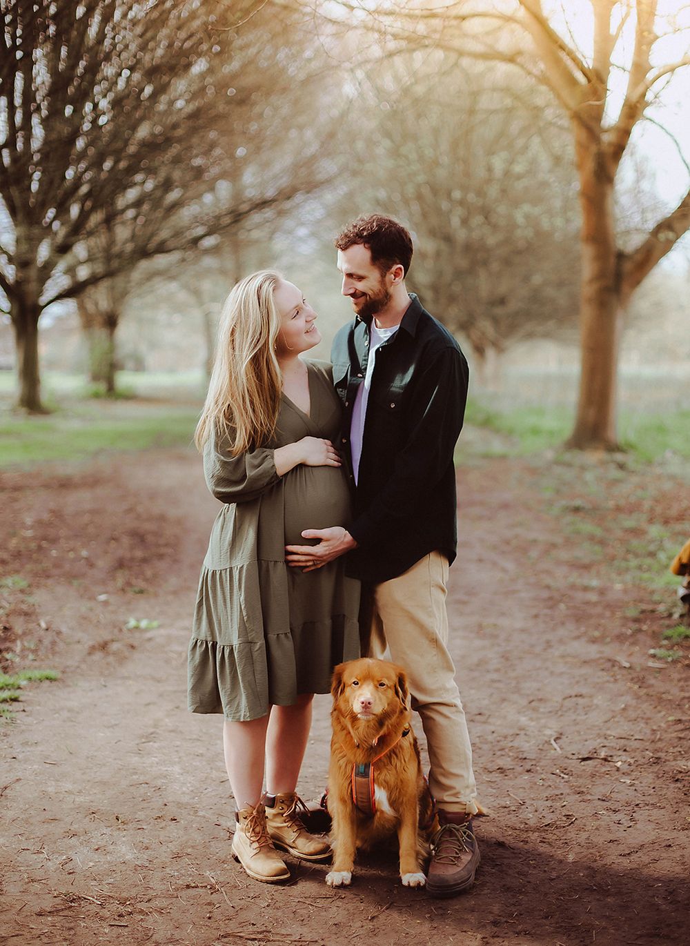 Couple and their golden retriever share a tender moment on a tree-lined path during golden hour.