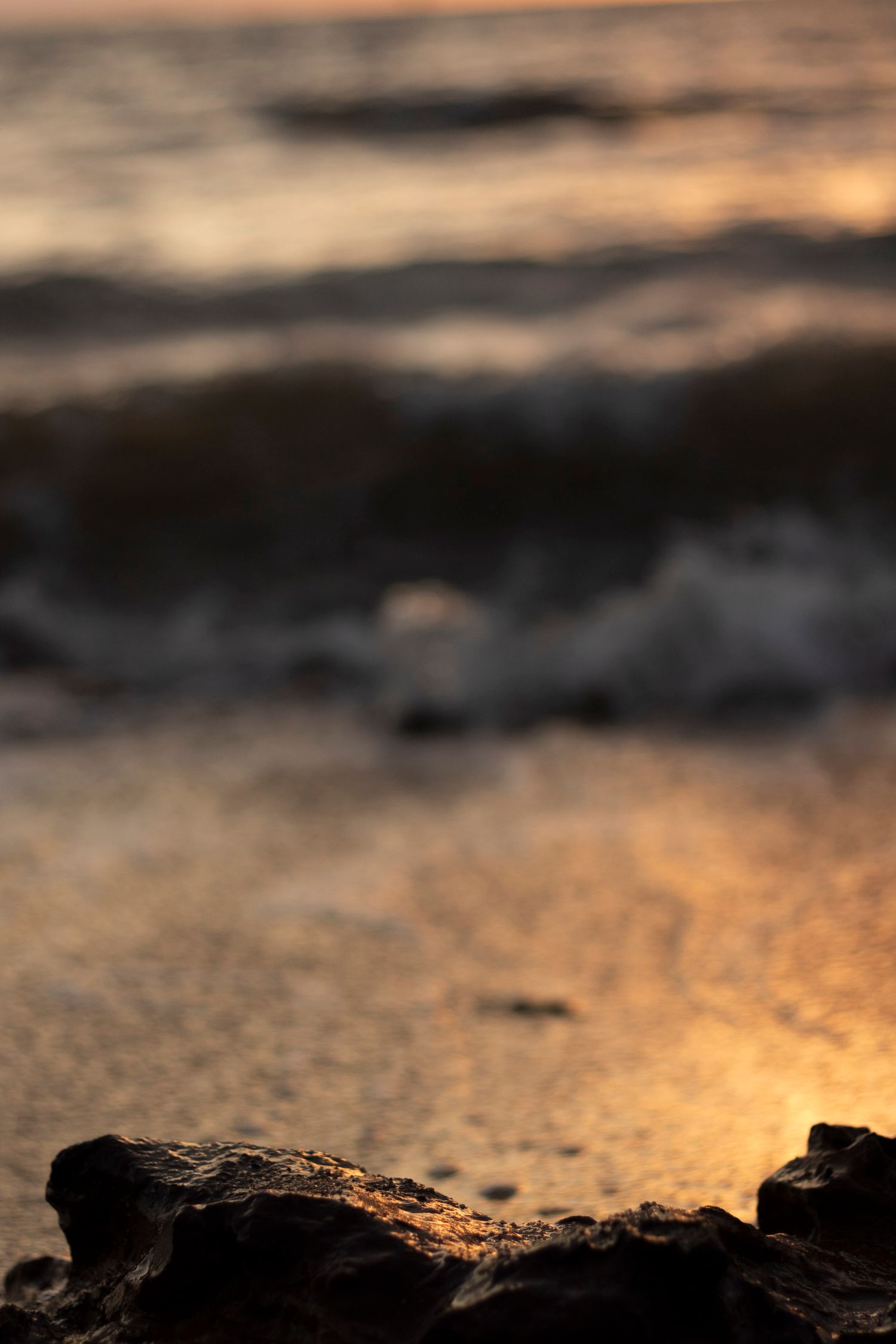 Dramatic sunset seascape with dark rocks in foreground and golden light on water.