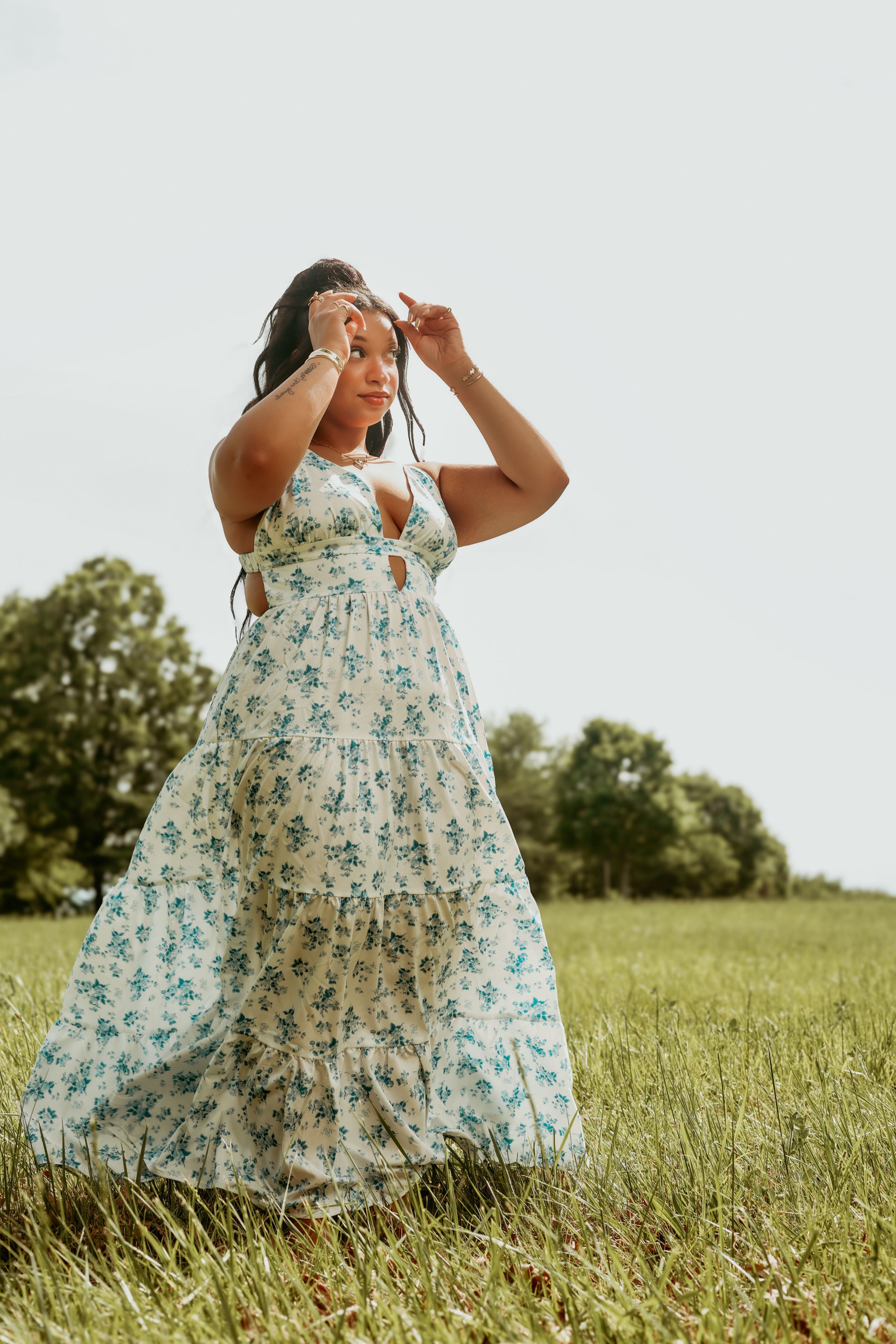 Woman in floral maxi dress standing in open green field outdoors.