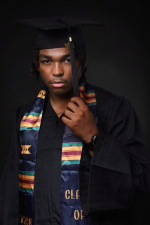 Young man in graduation cap and gown with colorful kente stole posing for a senior portrait.