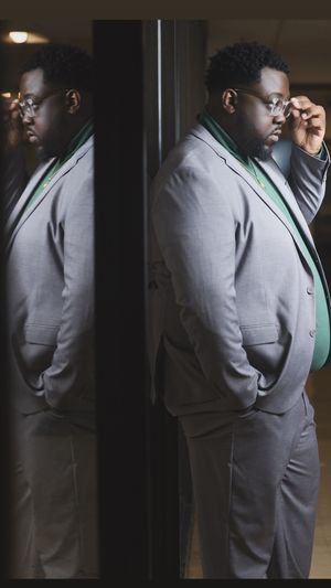 Stylish man in gray suit and glasses reflected in a mirror, creating a double portrait effect.