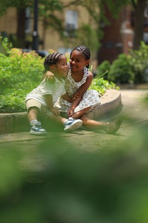 Two young children with braids sitting together on garden steps smiling.