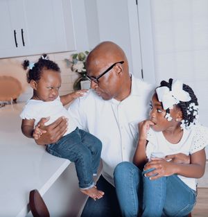 Loving grandfather in white shirt holding two young granddaughters in a bright modern kitchen setting.