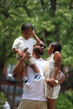 Happy family with father lifting young son while mother stands beside them in park.