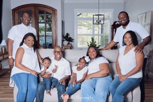 Large Black family in matching white tops and jeans posing together in a bright modern living room.
