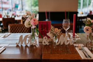 Wedding table setting featuring 'Mr & Mrs' letters, pink floral centerpieces, wine glasses and rustic wooden decor.