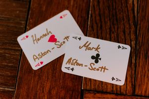 Two playing cards showing handwritten names serve as place cards or escort cards on a wooden table surface.