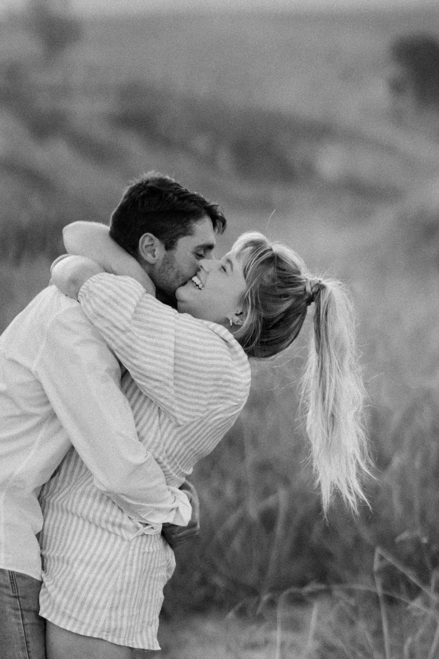 A romantic black and white photograph of a couple embracing and laughing together in a field.