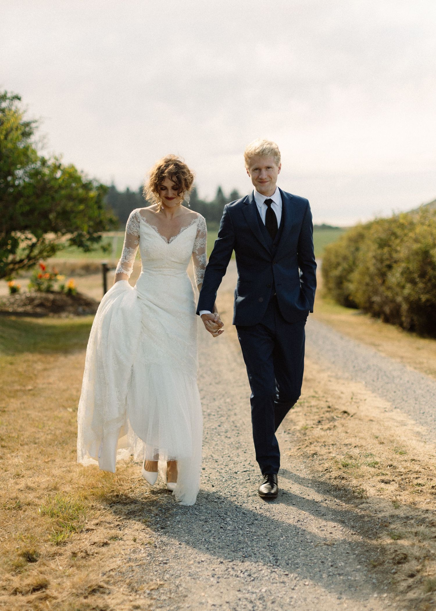 Wedding couple walking together on a gravel path through a scenic countryside setting.