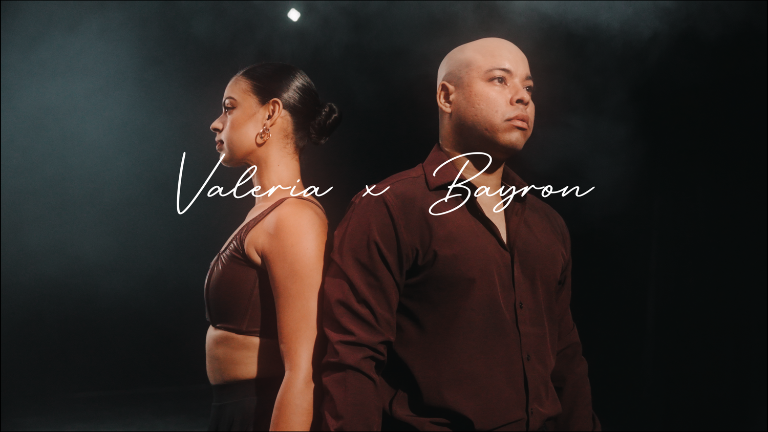 Two performers stand back-to-back under dramatic lighting for an artistic photoshoot.