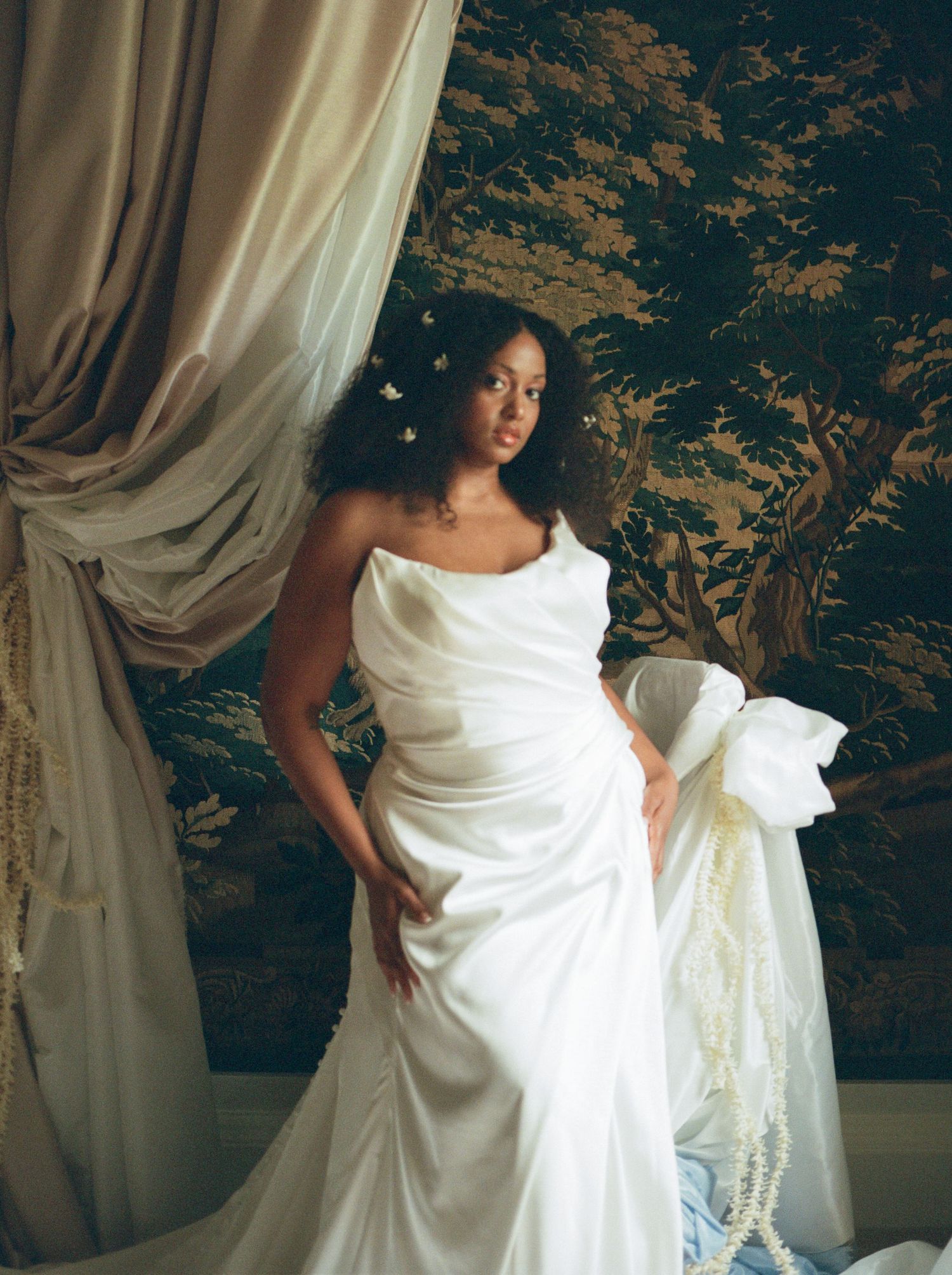 Two people in a sunlit room preparing a white wedding dress before the ceremony.