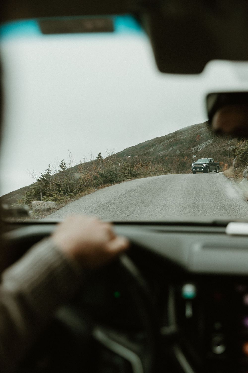 Scenic mountain road view captured through a car's windshield on a misty day.