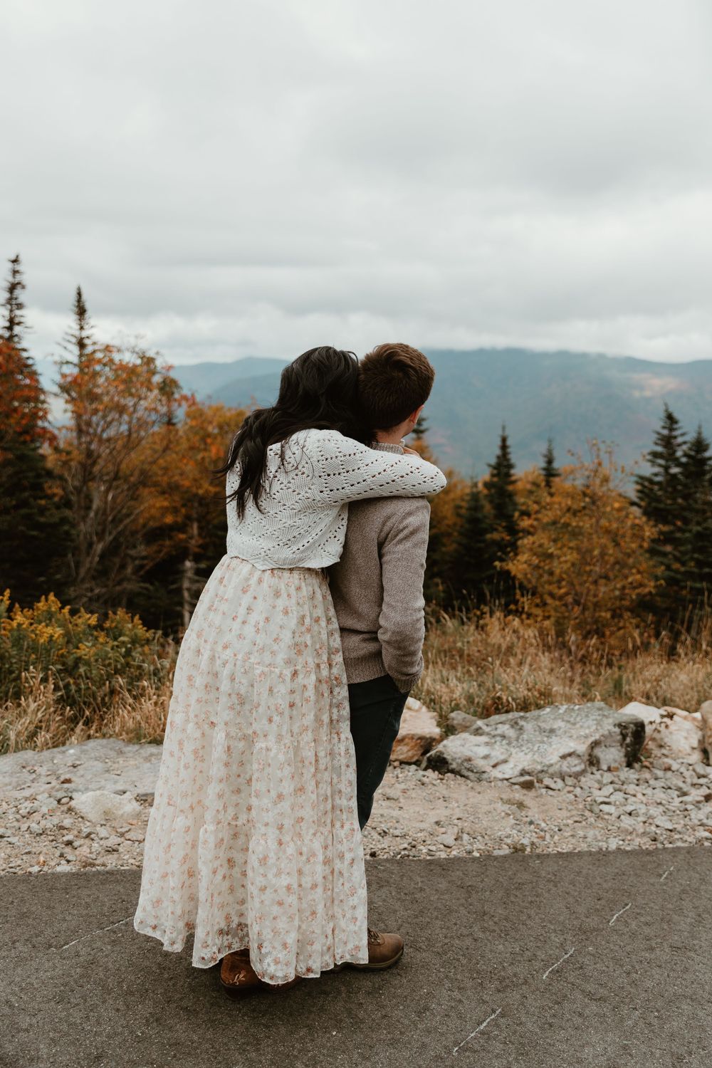 Intimate moment shared on mountain path with autumn foliage in background.