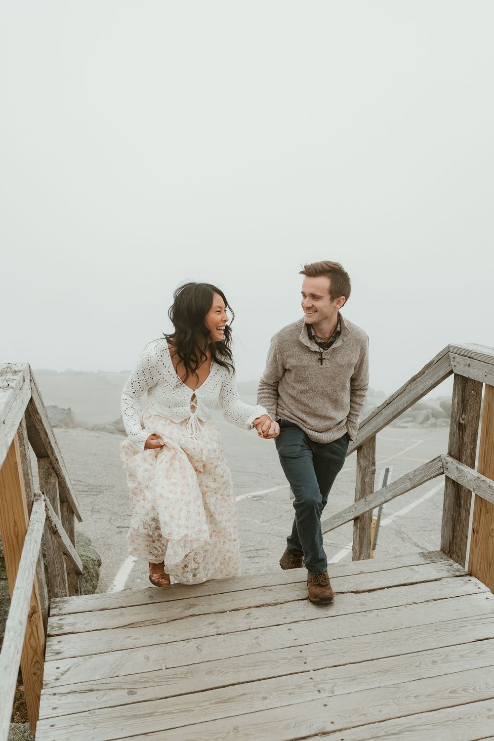 Couple enjoying a playful moment on wooden stairs in foggy weather.