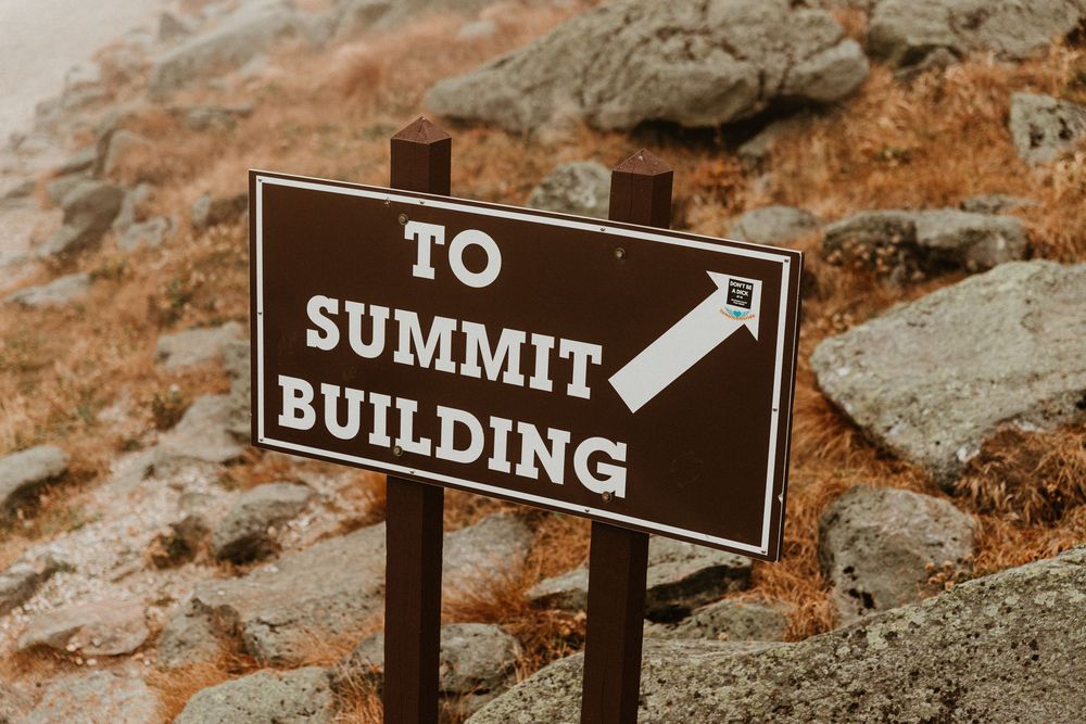 Brown directional signs on rocky terrain pointing towards summit.