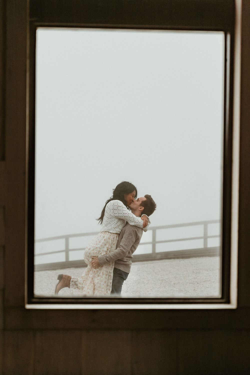 Romantic moment captured through observation deck windows with foggy background.