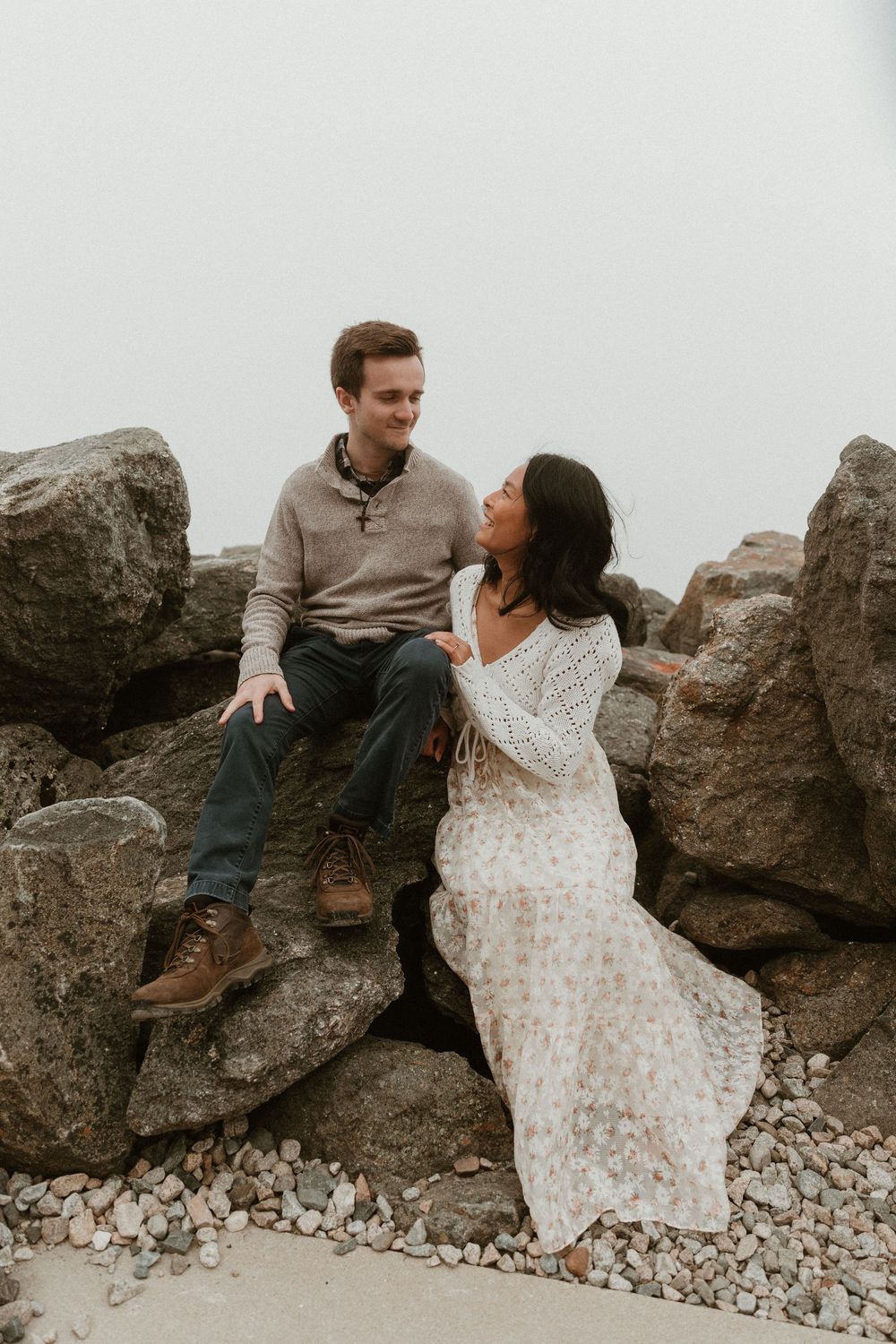 Couple sitting on rocky outcrop during foggy mountain photoshoot.