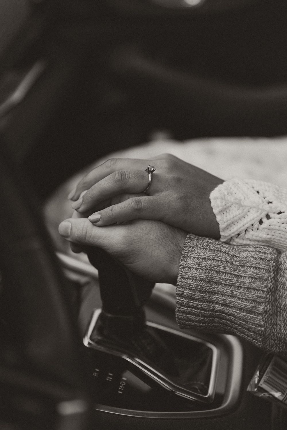 Close-up of hands resting on car steering wheel wearing knit sweater sleeves.