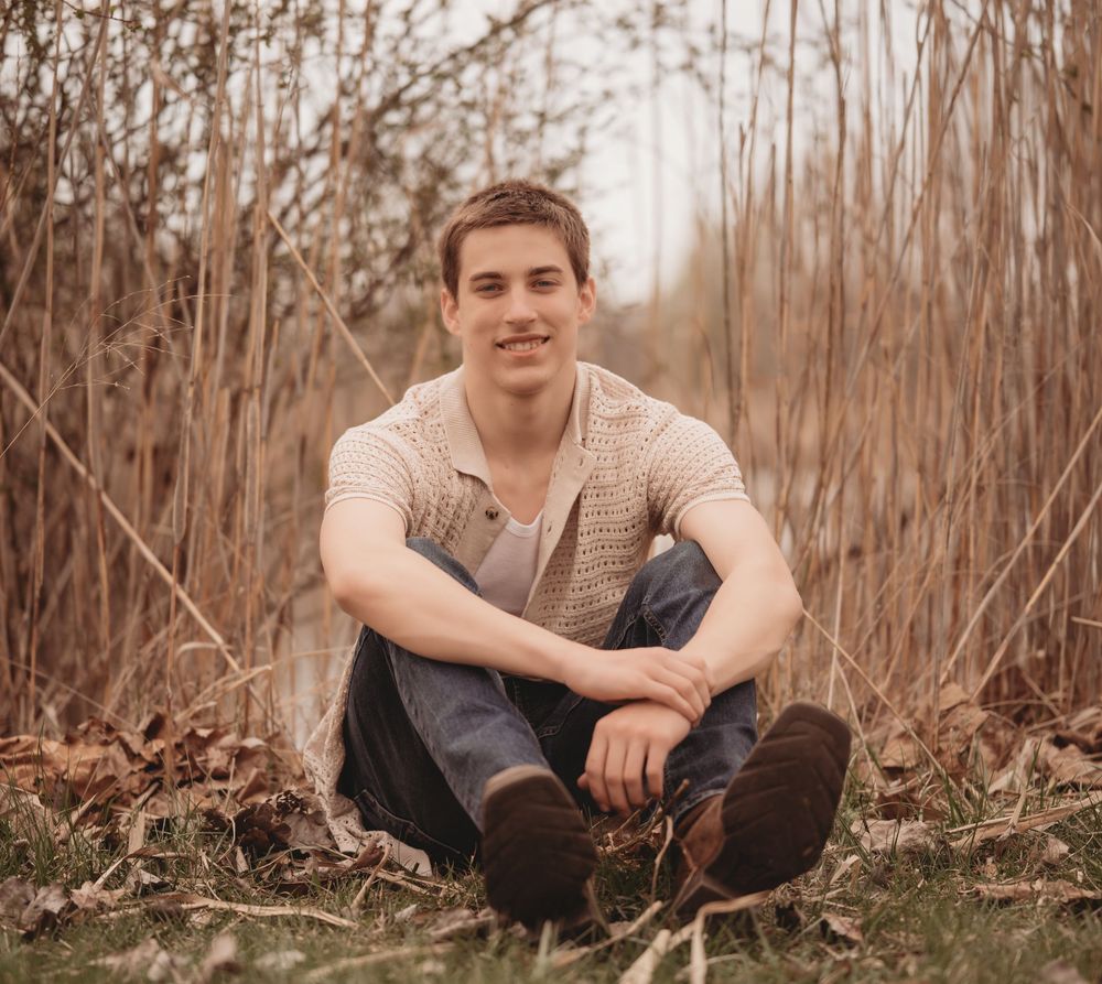 Person in beige sweater sits cross-legged among tall autumn grasses in soft natural lighting.