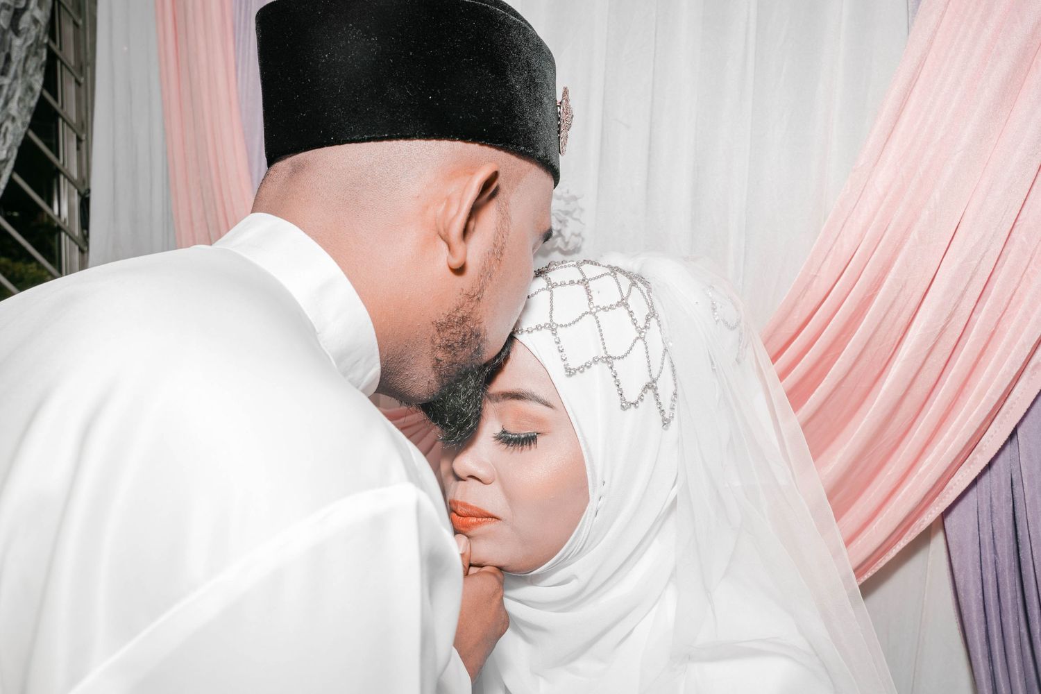 Intimate wedding moment captured against pink and white draped backdrop.