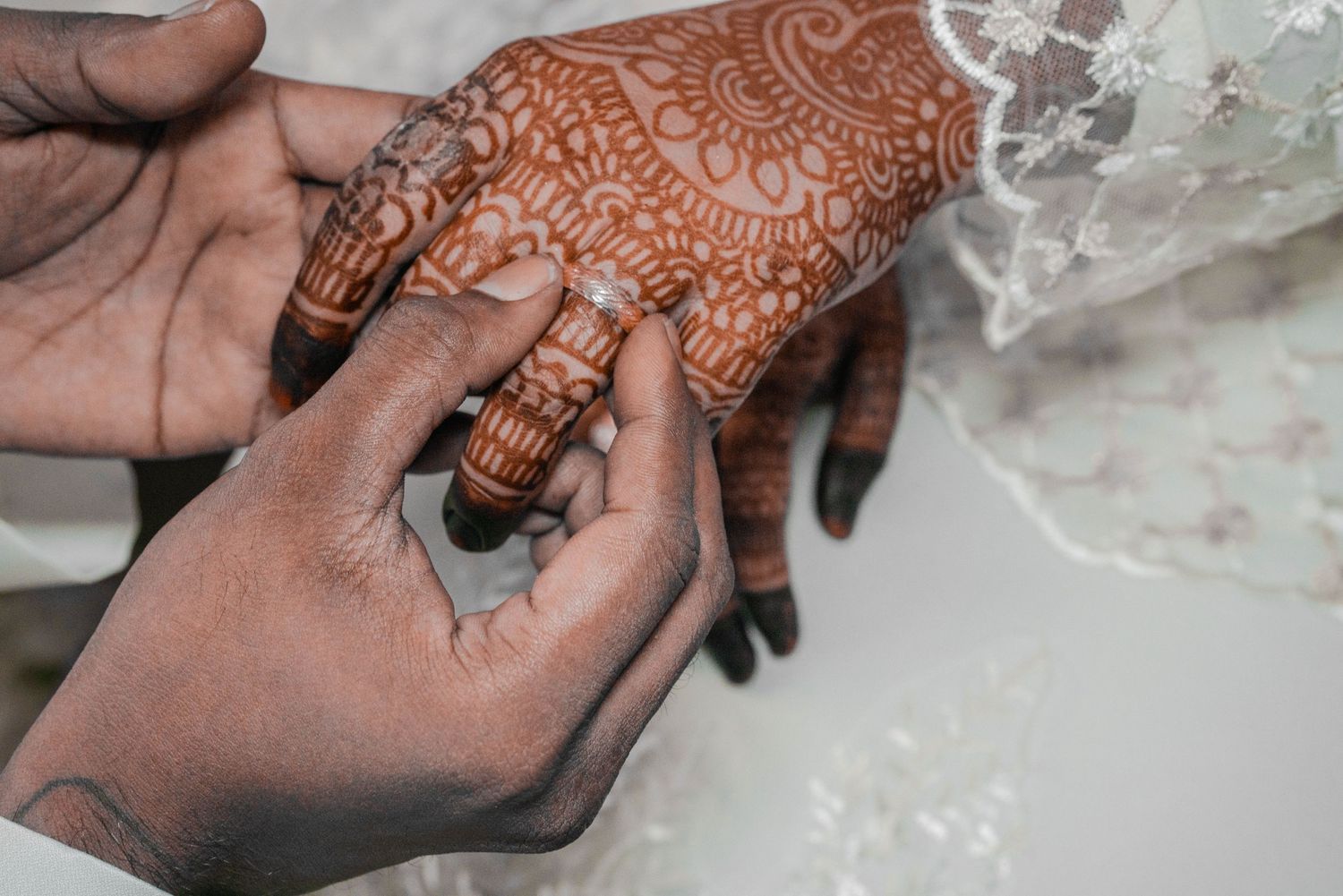 Close-up of intricate henna design being applied to hands during traditional wedding ceremony.