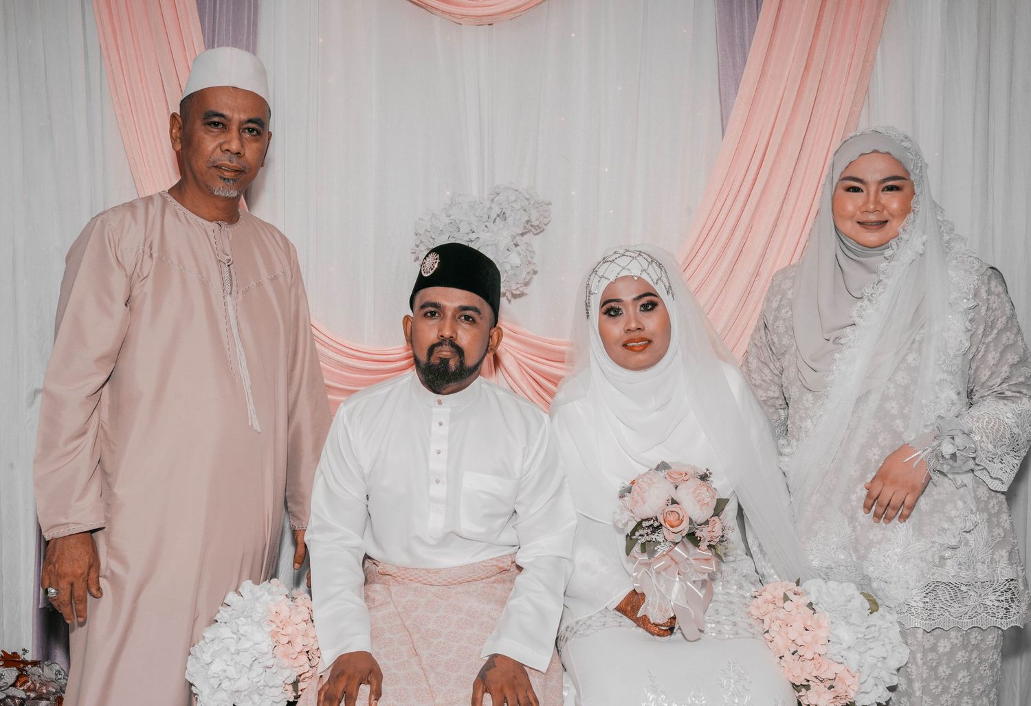 Wedding group photo with traditional attire against floral decorated backdrop.