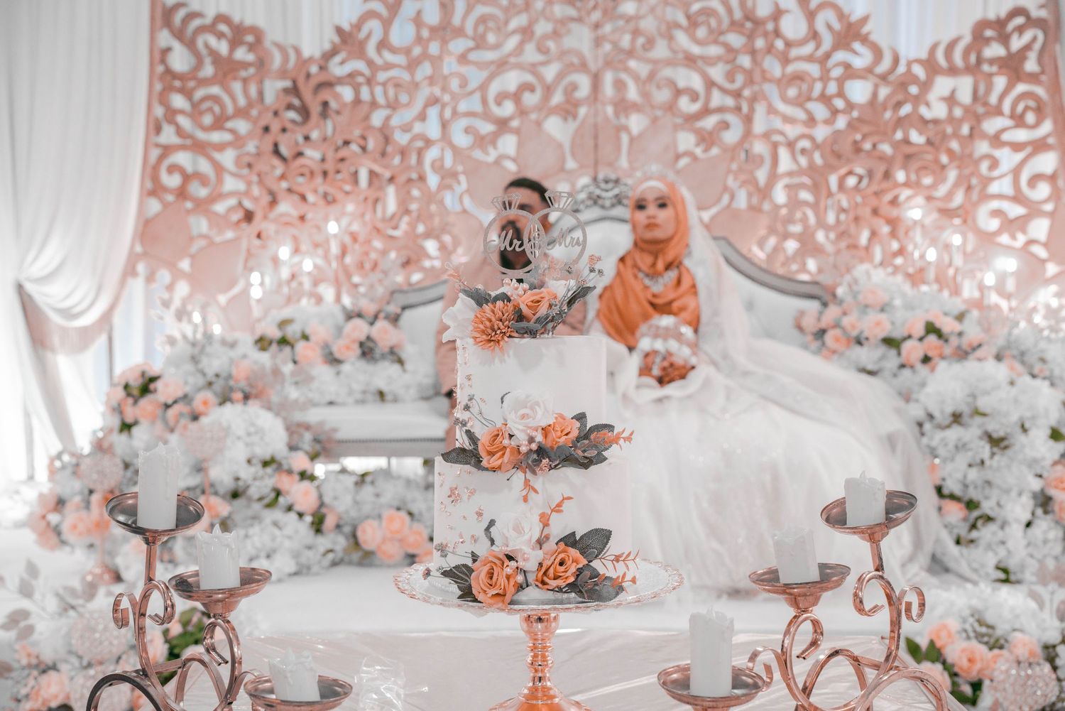 Elegant wedding cake display with coral and white floral decorations against intricate backdrop.