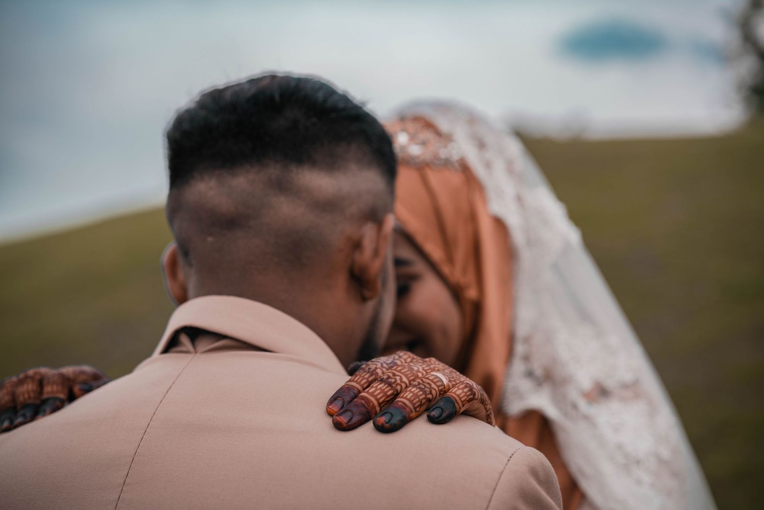 A tender wedding moment as a bride gently places her hand on the groom's shoulder in a peach-colored suit.