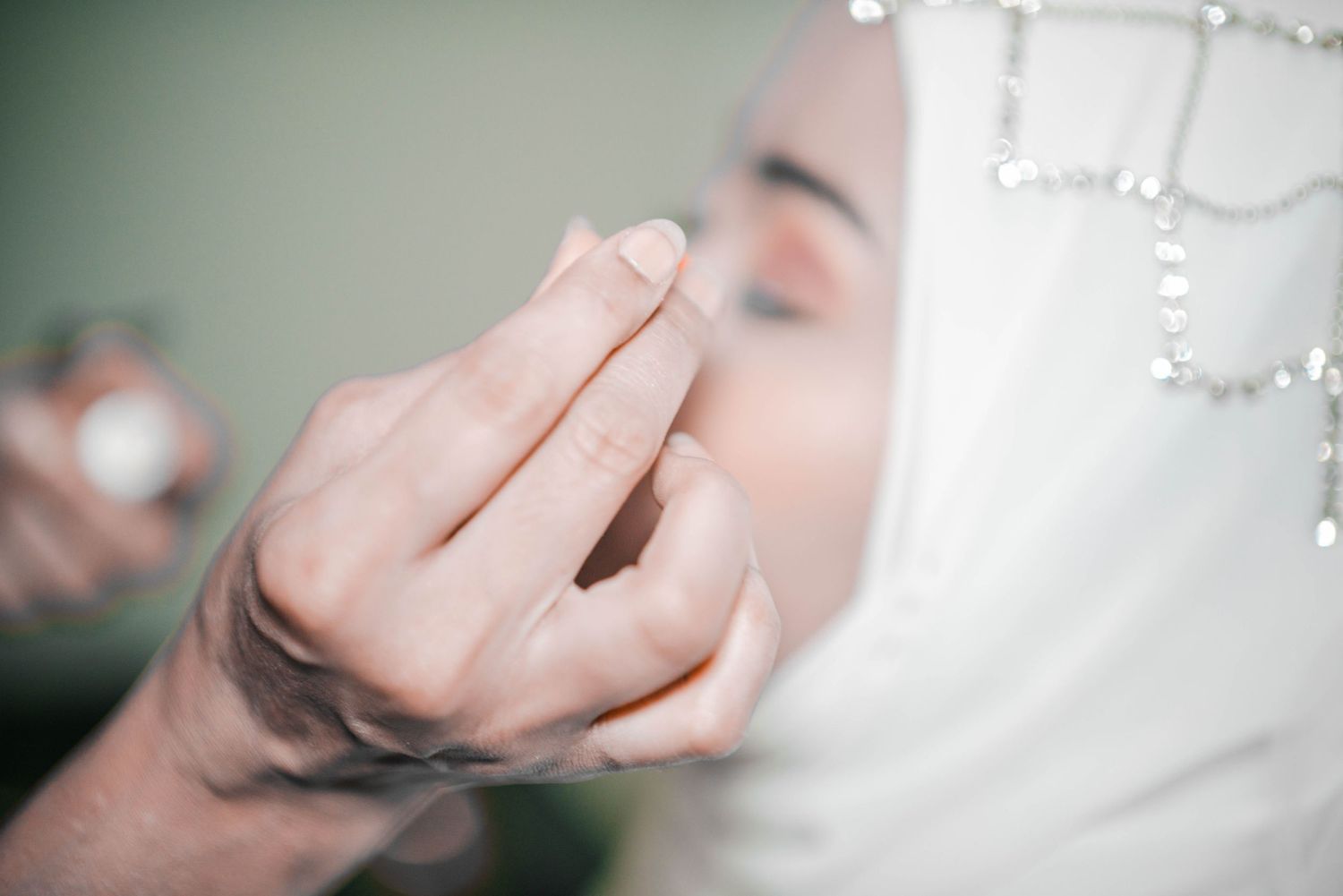 Close-up shot of wedding makeup application with pearl-adorned white hijab.