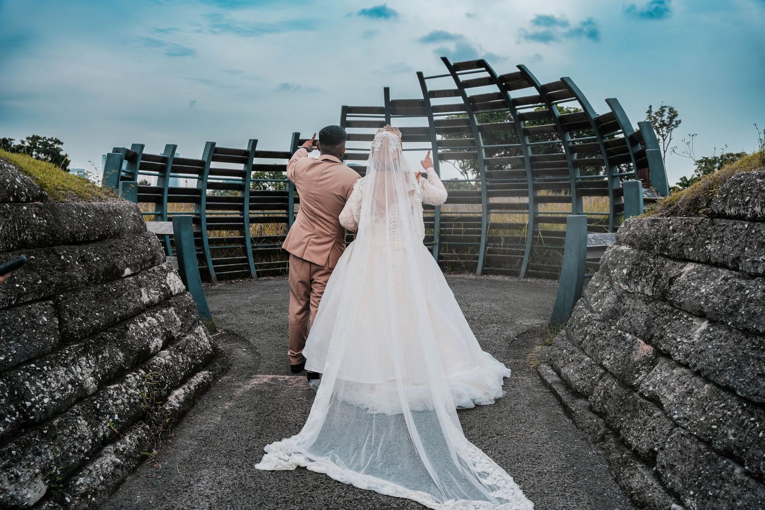 A couple in wedding attire walking through an architectural archway with a flowing white veil.