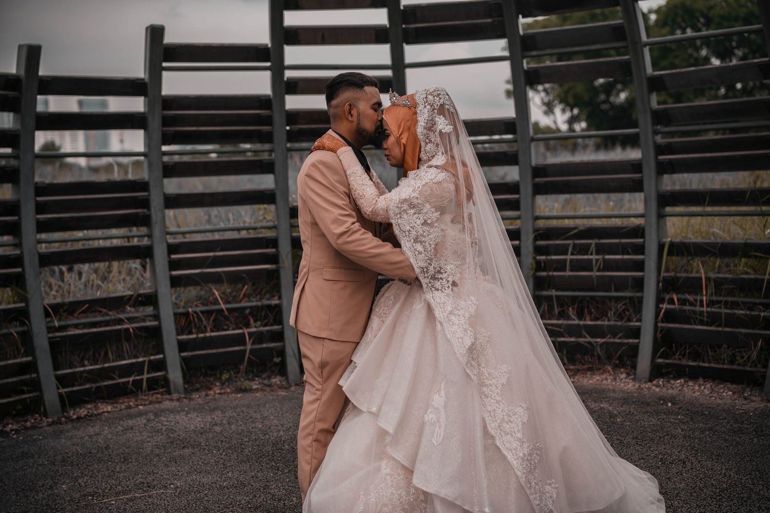 A romantic wedding moment under a wooden lattice structure with a bride in white and groom in tan.