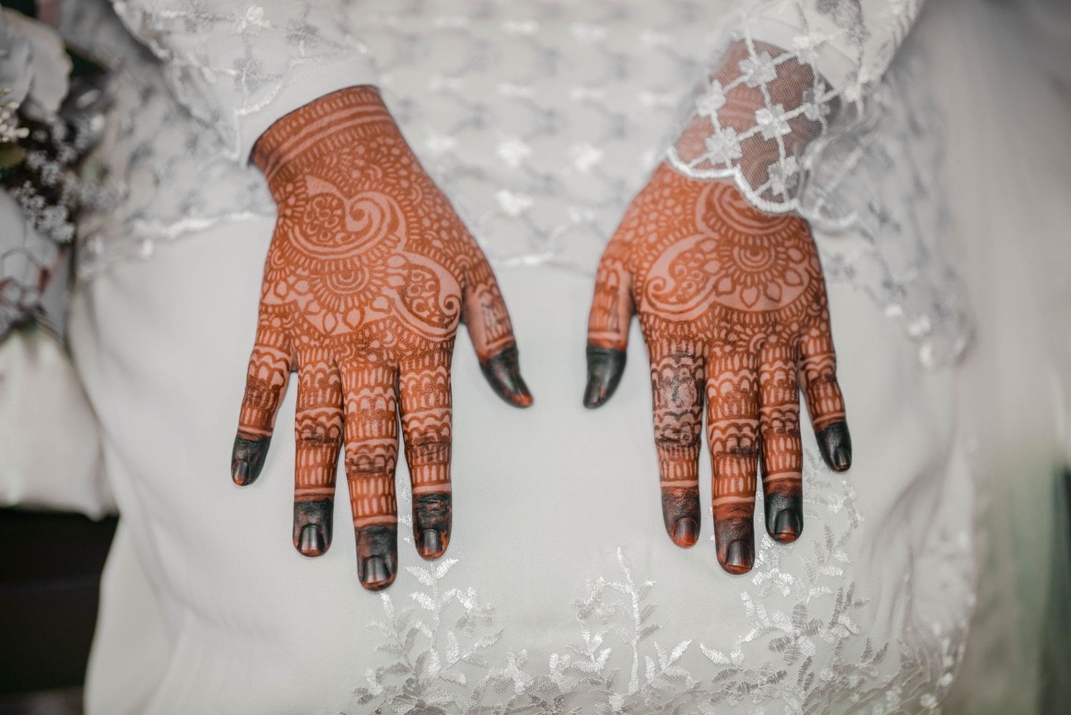 Close-up of intricate henna mehndi designs on both hands against white lace.