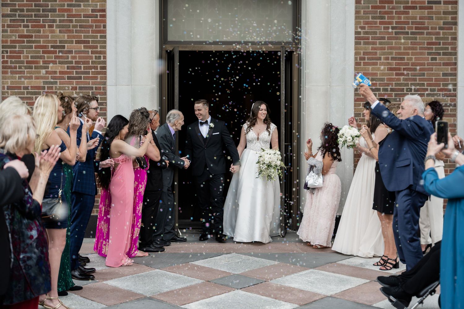 Wedding guests shower a couple with confetti as they exit a brick church building at a Chicago Wedding.