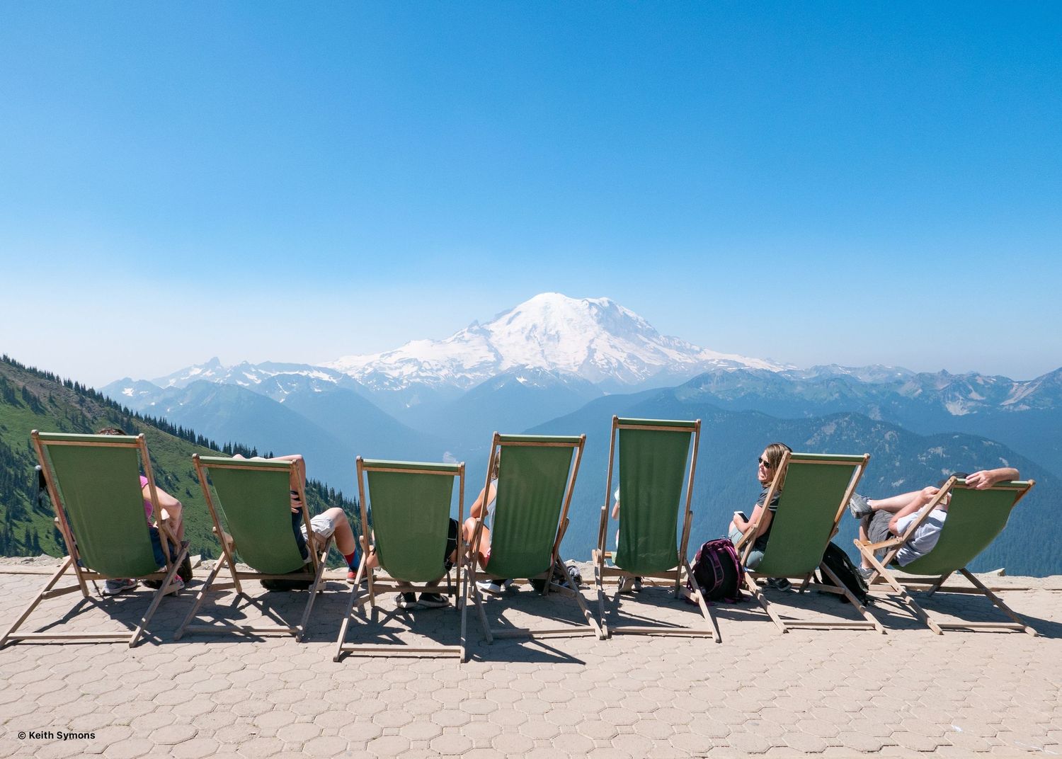 Row of green lounge chairs overlooking snow-capped Mount Rainier on a clear day.