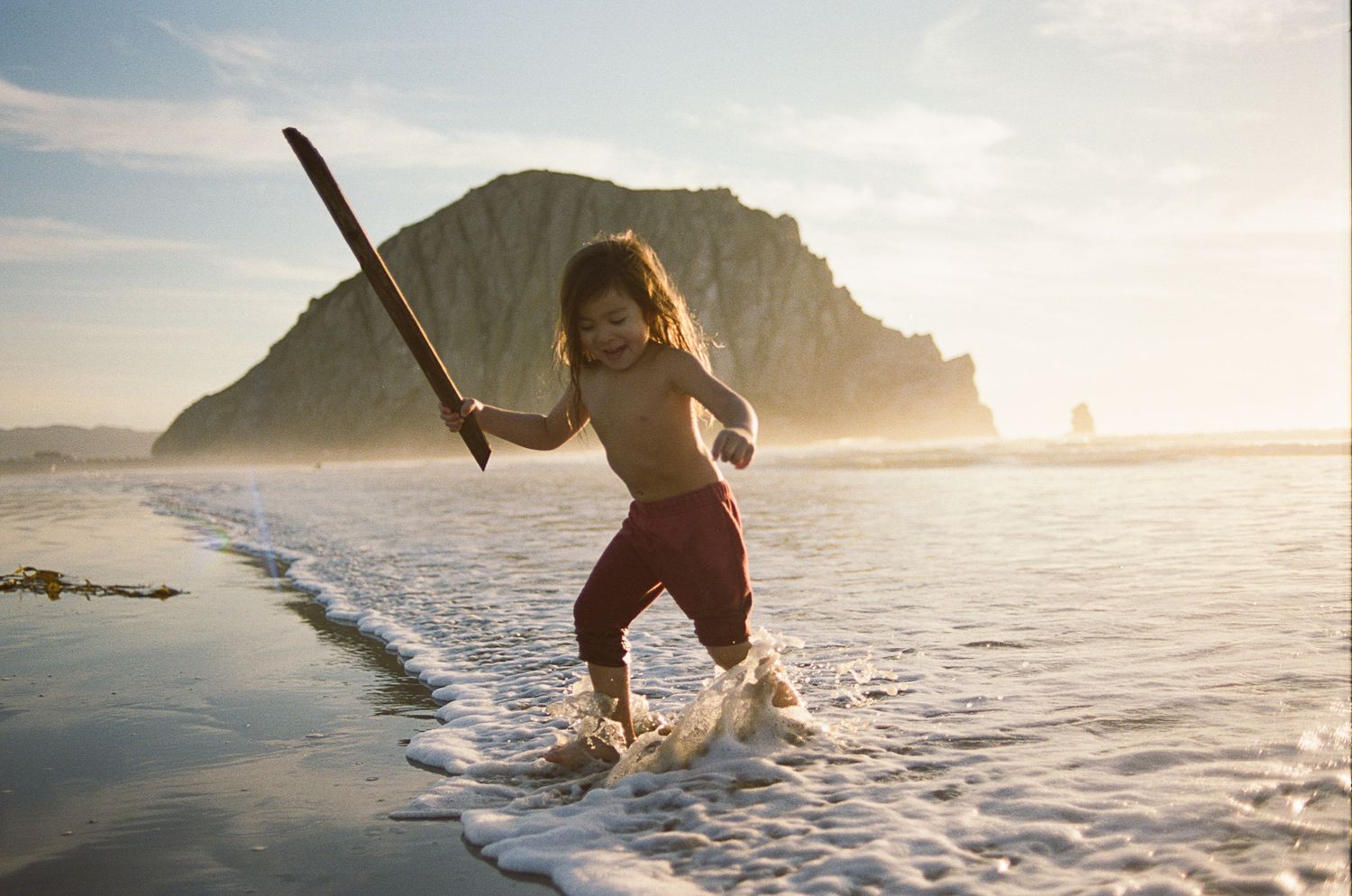 People enjoying water activities at a scenic beach with dramatic cliffs and golden sunlight.