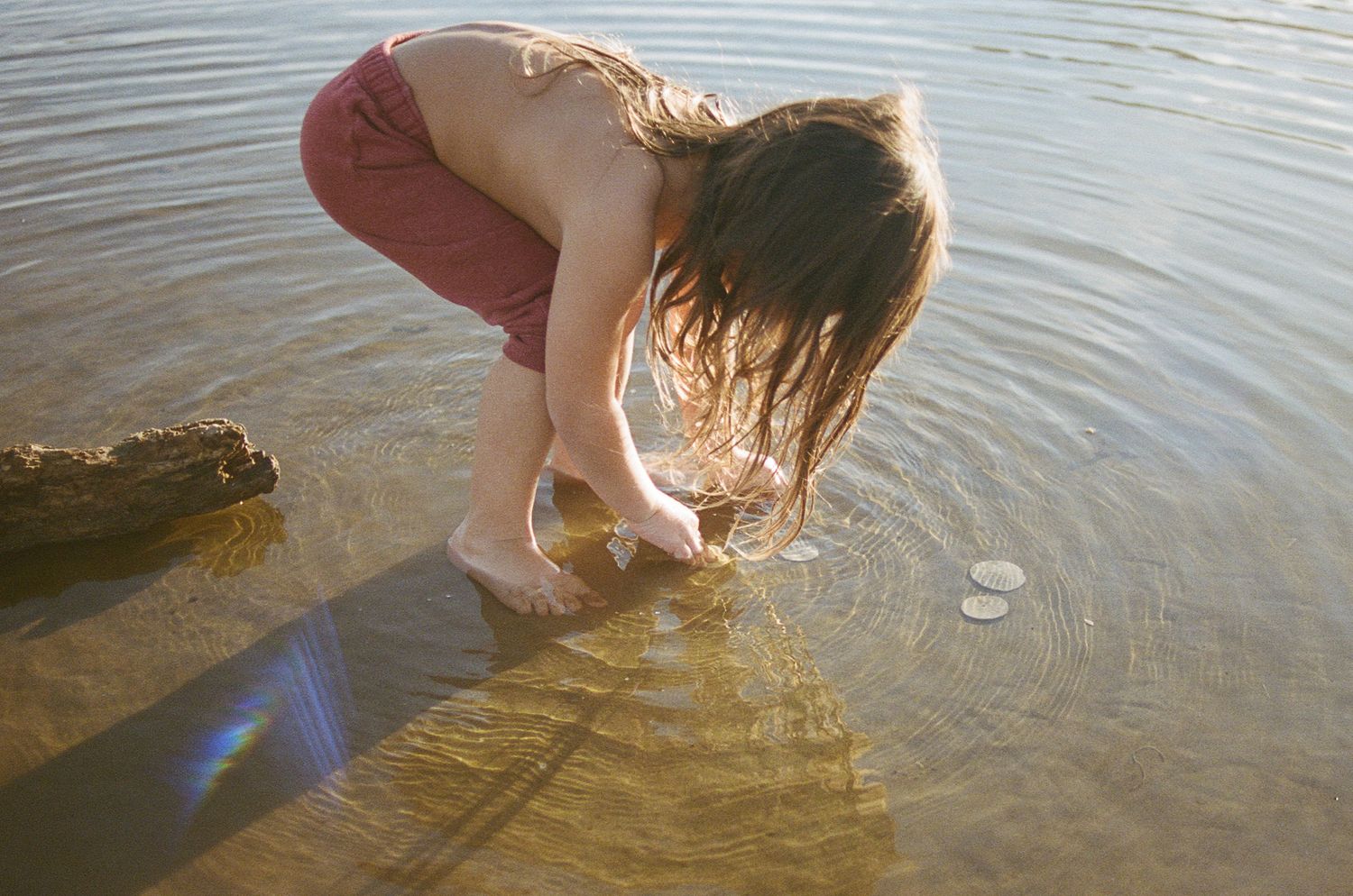 Close-up shot of hands splashing in shallow coastal waters during golden hour.