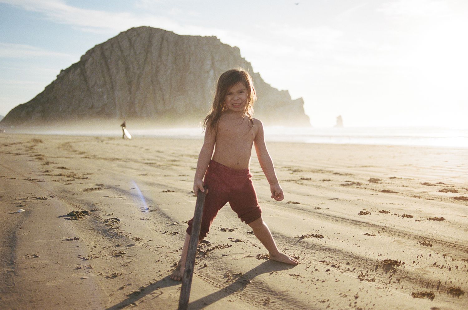Beachgoers explore a sandy shoreline with dramatic cliffs in the background during sunset.