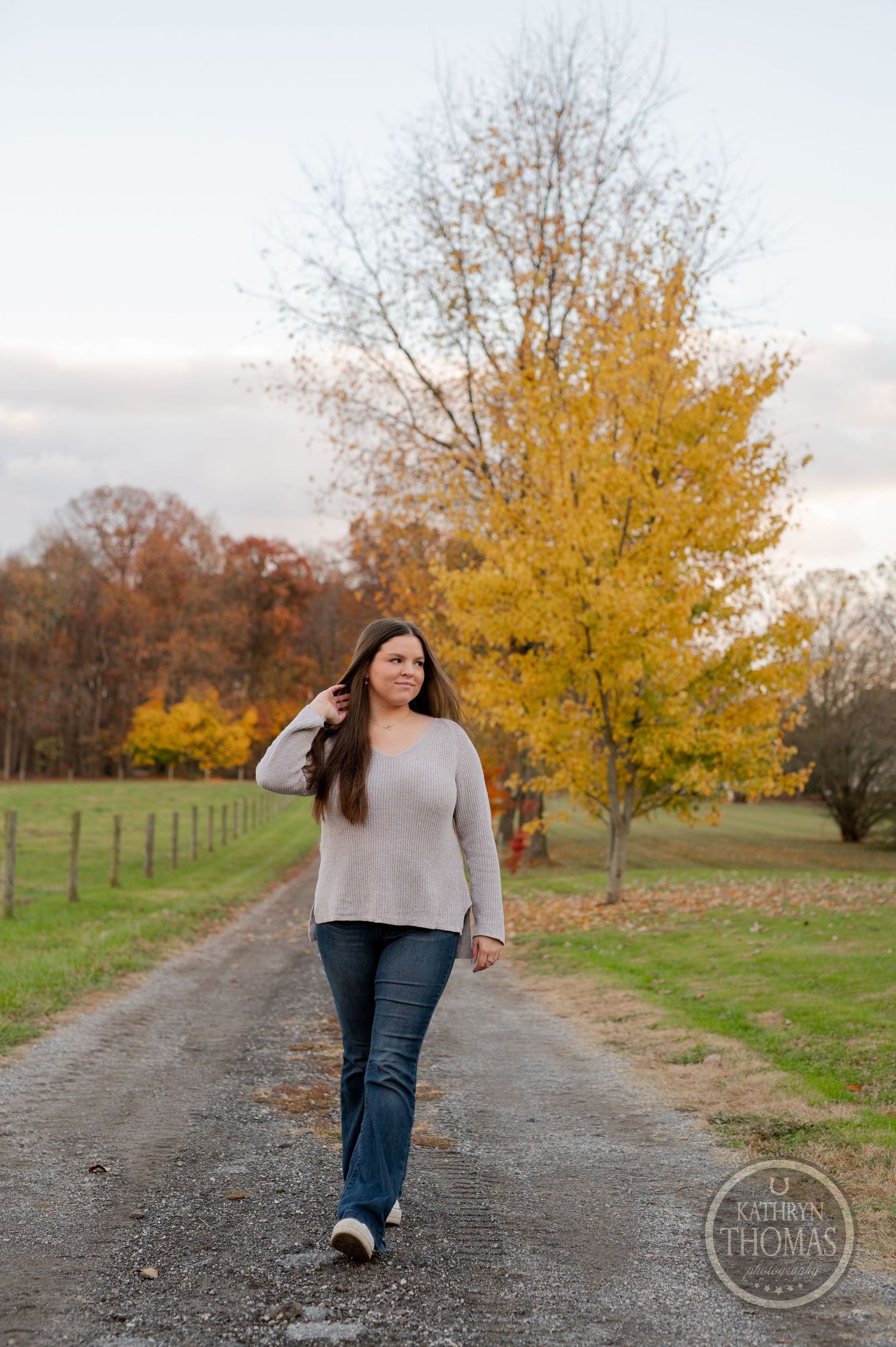 A person walks along a country path beneath vibrant yellow fall foliage.