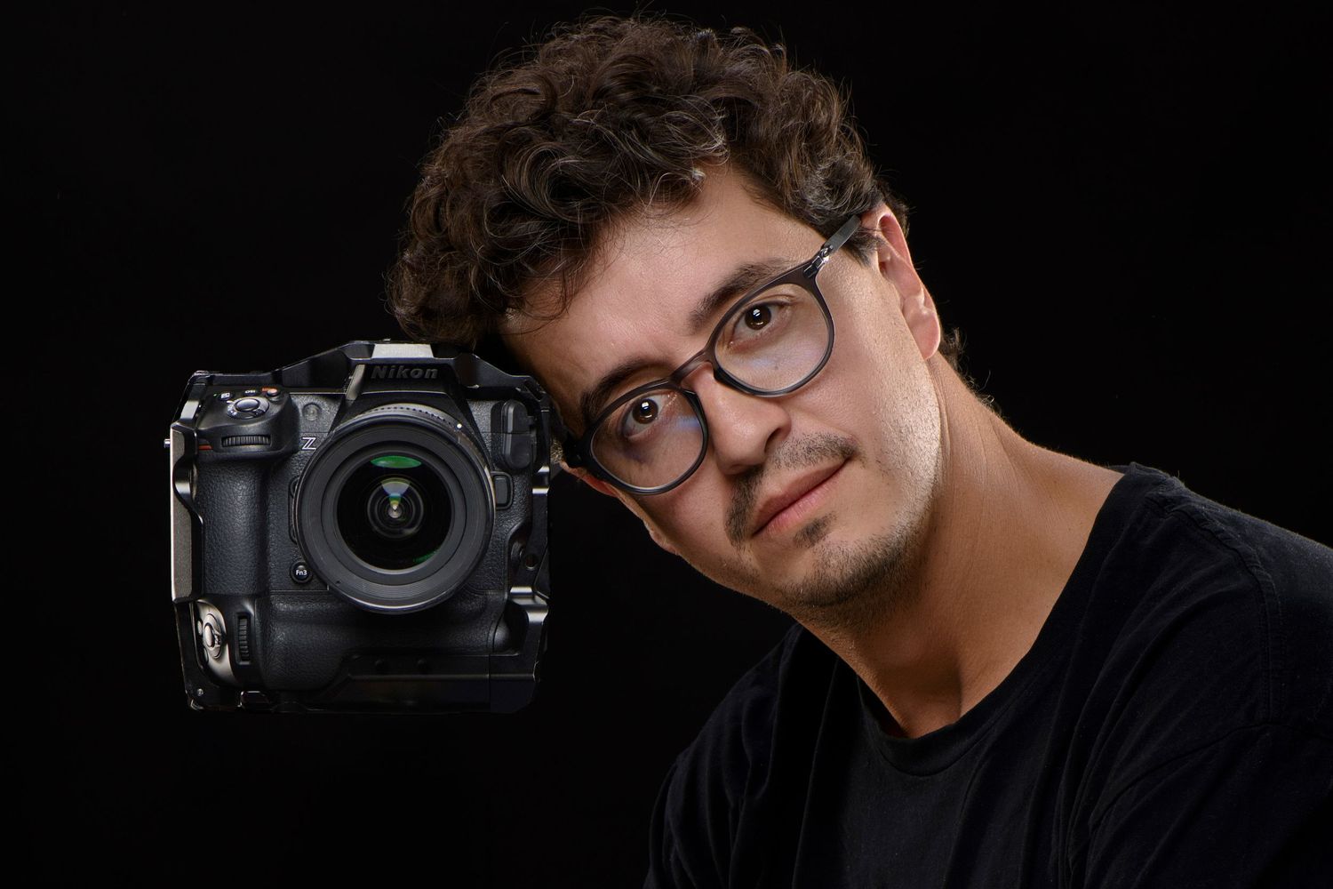 A young professional wearing glasses smiles warmly next to a QR code with a cup icon against a white backdrop.