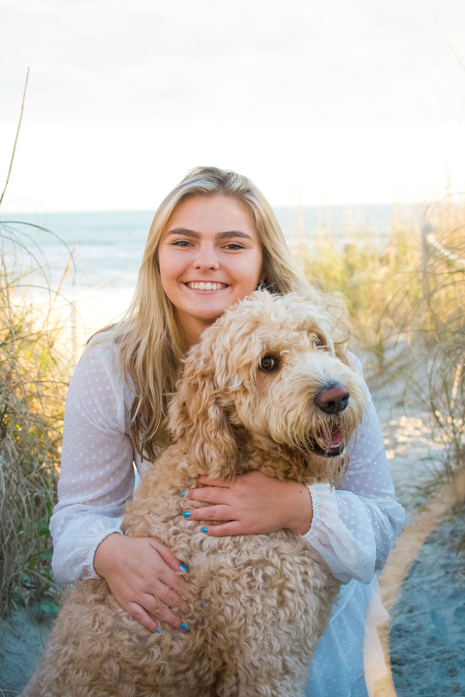A person embraces a fluffy goldendoodle dog on a sandy beach path.