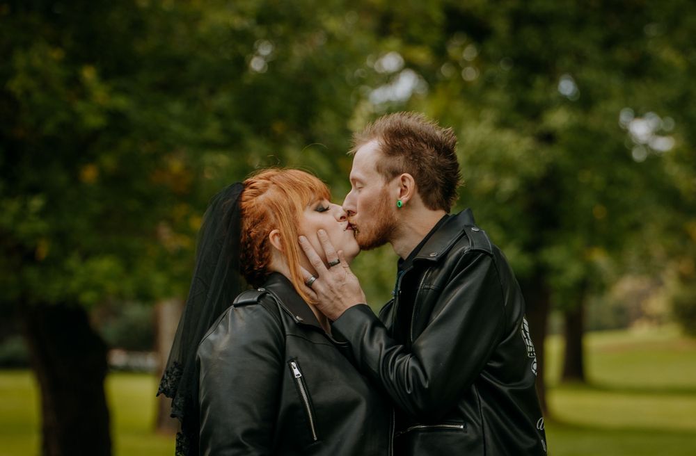 A romantic couple sharing an intimate kiss while wearing leather jackets in a park setting.