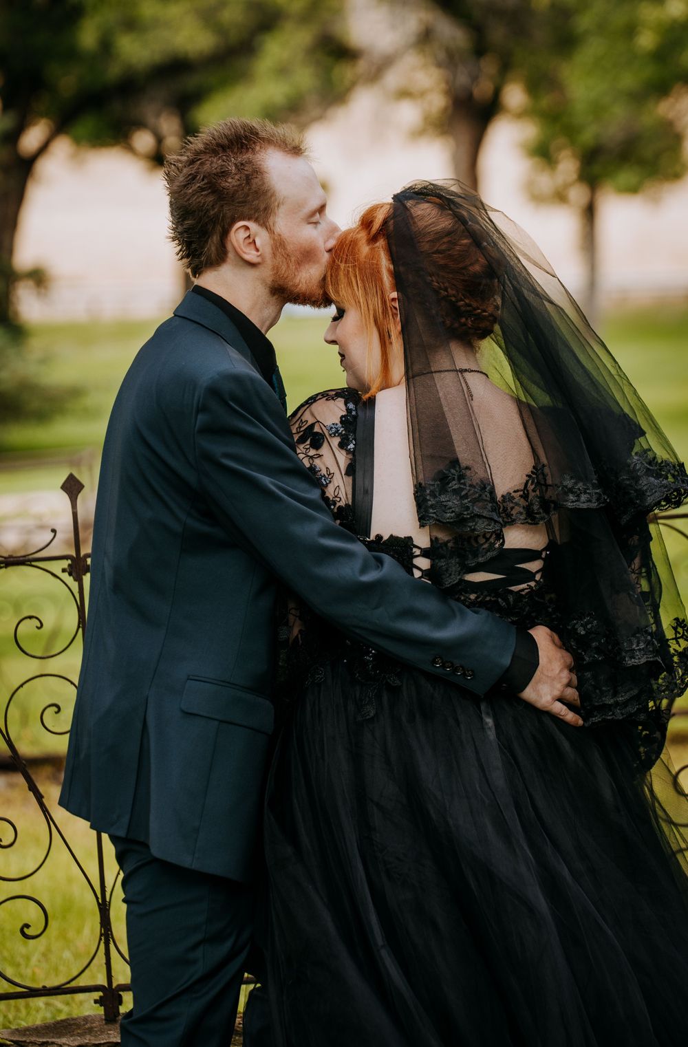A tender moment between newlyweds with the bride wearing a dramatic black wedding gown and veil.