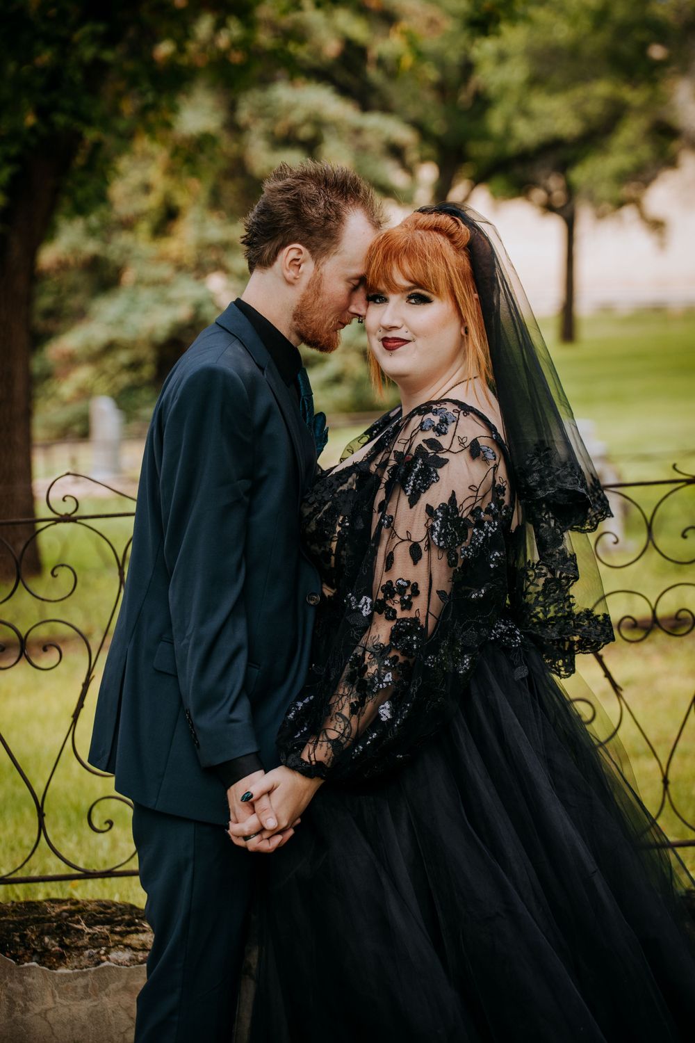 A romantic wedding portrait against a brick wall featuring a black lace dress and elegant styling.