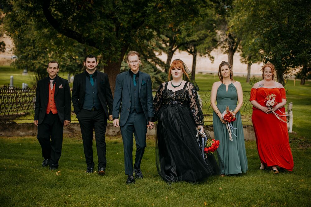 Wedding party poses together outdoors with the couple and guests wearing mix of formal attire.