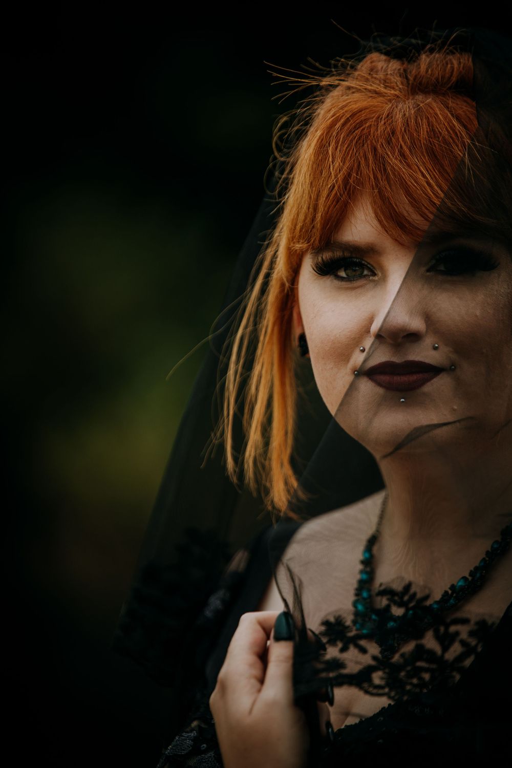 Moody close-up portrait with black veil and gothic makeup against dark background.