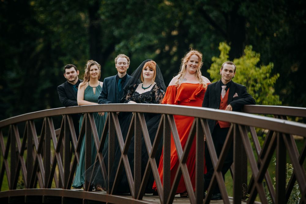 Wedding party in formal attire poses on wooden bridge in natural setting.