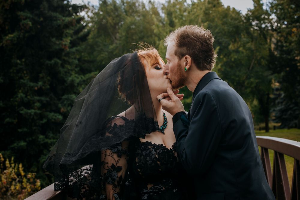 An intimate moment between newlyweds sharing a kiss on a wooden bridge.
