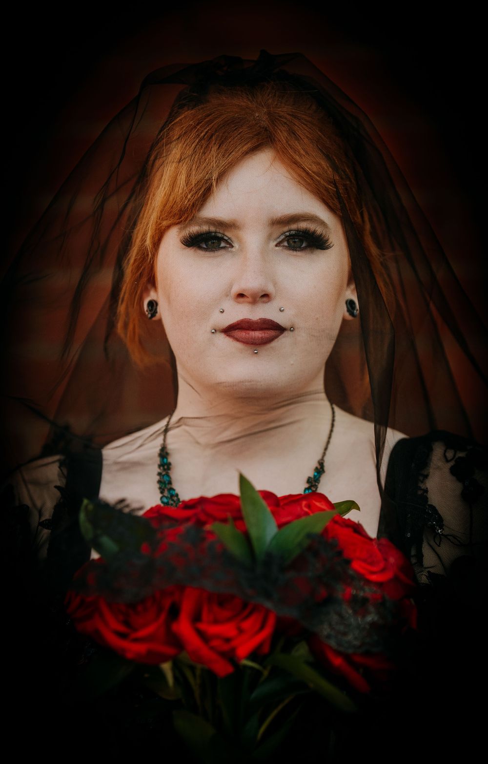 Gothic bride holding red roses in dark aesthetic portrait with dramatic lighting and black lace dress.