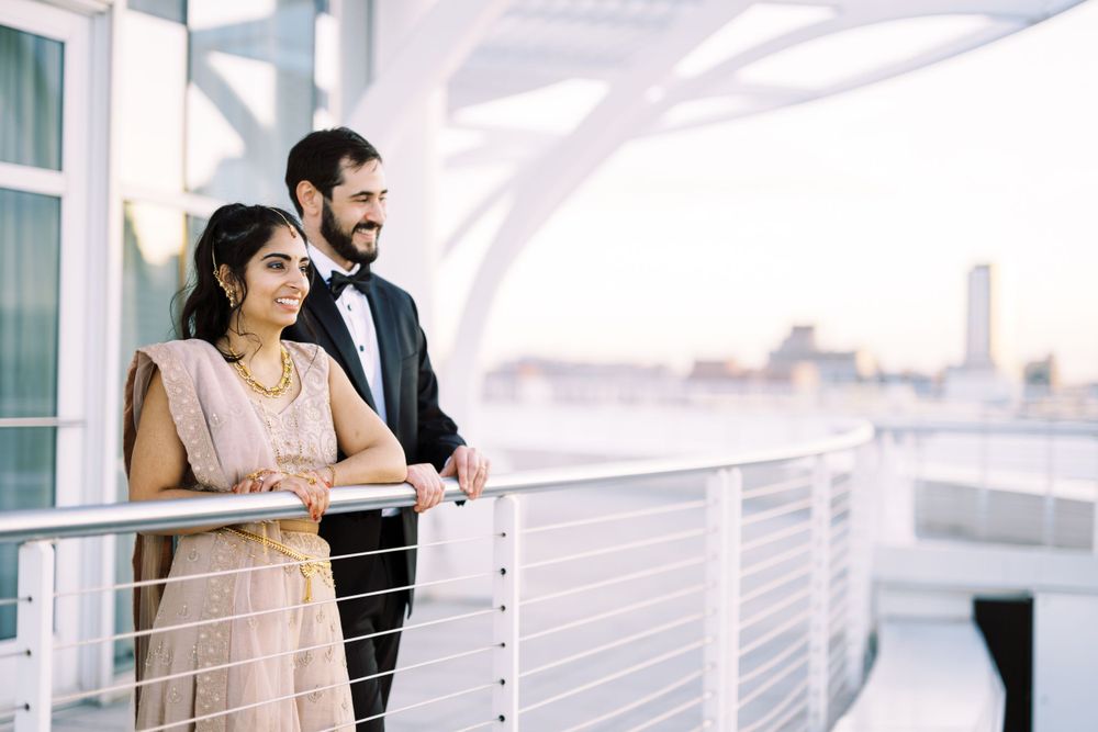 A couple in formal attire shares a tender moment on a balcony overlooking a city skyline during golden hour.
