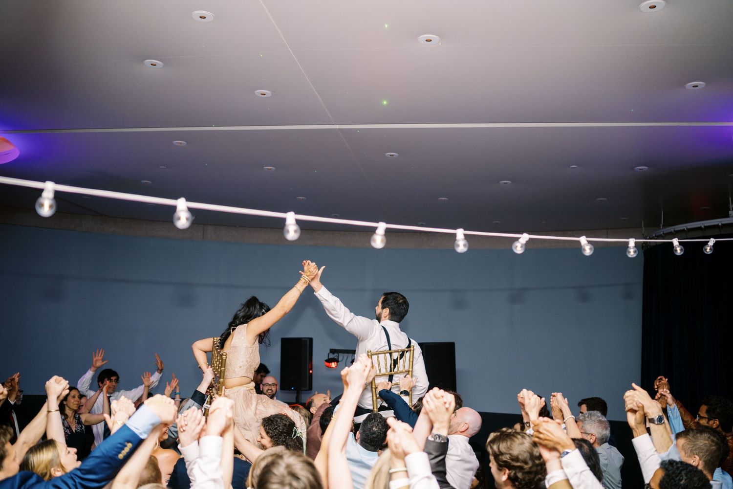A celebratory moment at a reception as a couple raises their joined hands above a cheering crowd.